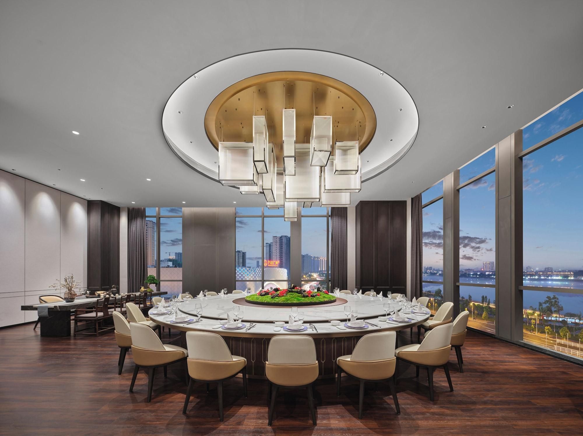 A modern conference room with a round table, chairs, a chandelier, and large windows with a city view.