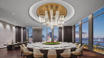 A modern conference room with a round table, chairs, a chandelier, and large windows with a city view.