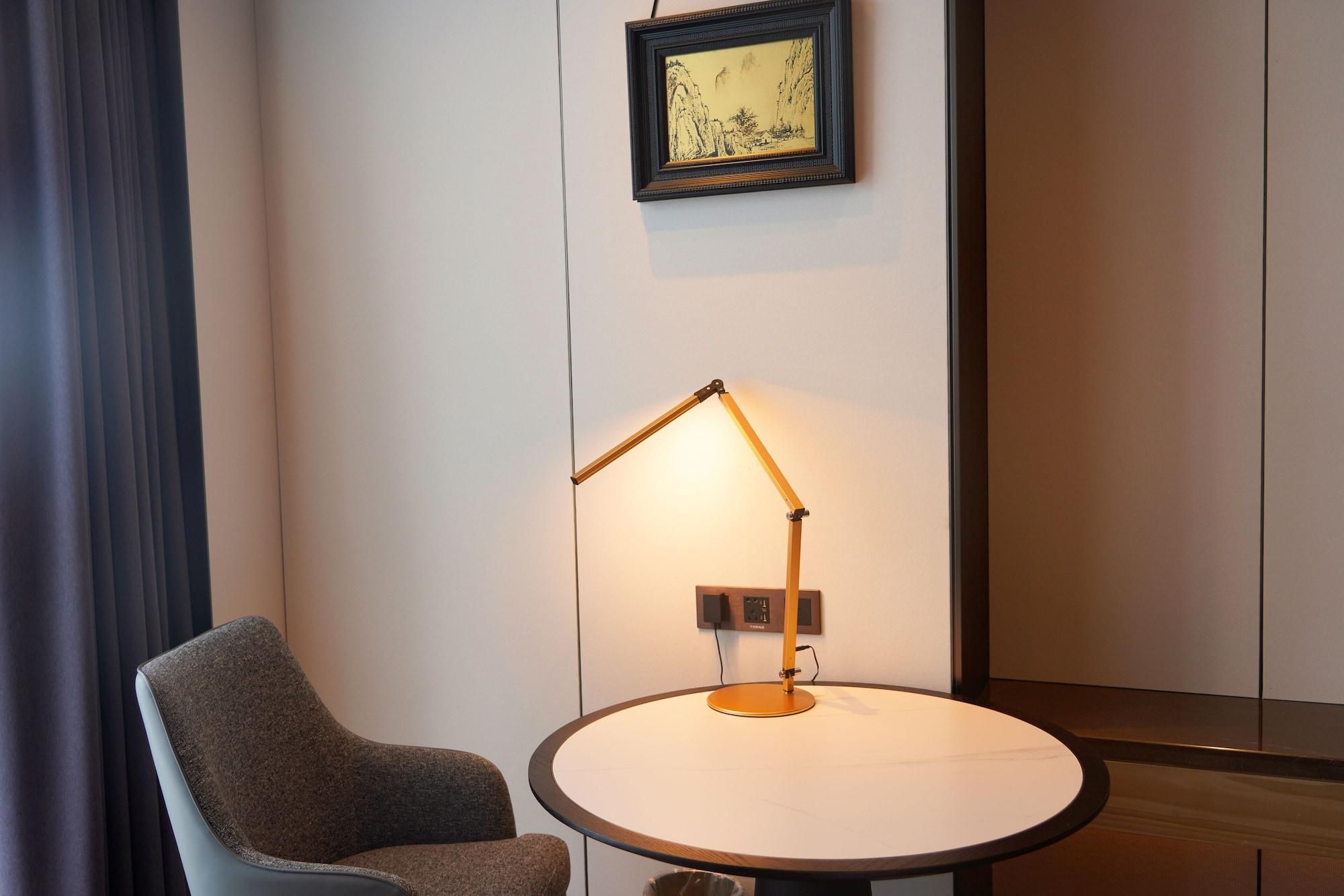 Una habitación moderna con una mesa redonda, una silla, una lámpara de pie y una obra de arte enmarcada en la pared.