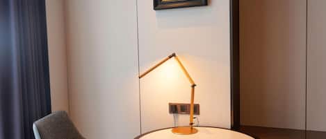 A modern room with a round table, a chair, a floor lamp, and a framed artwork on the wall.