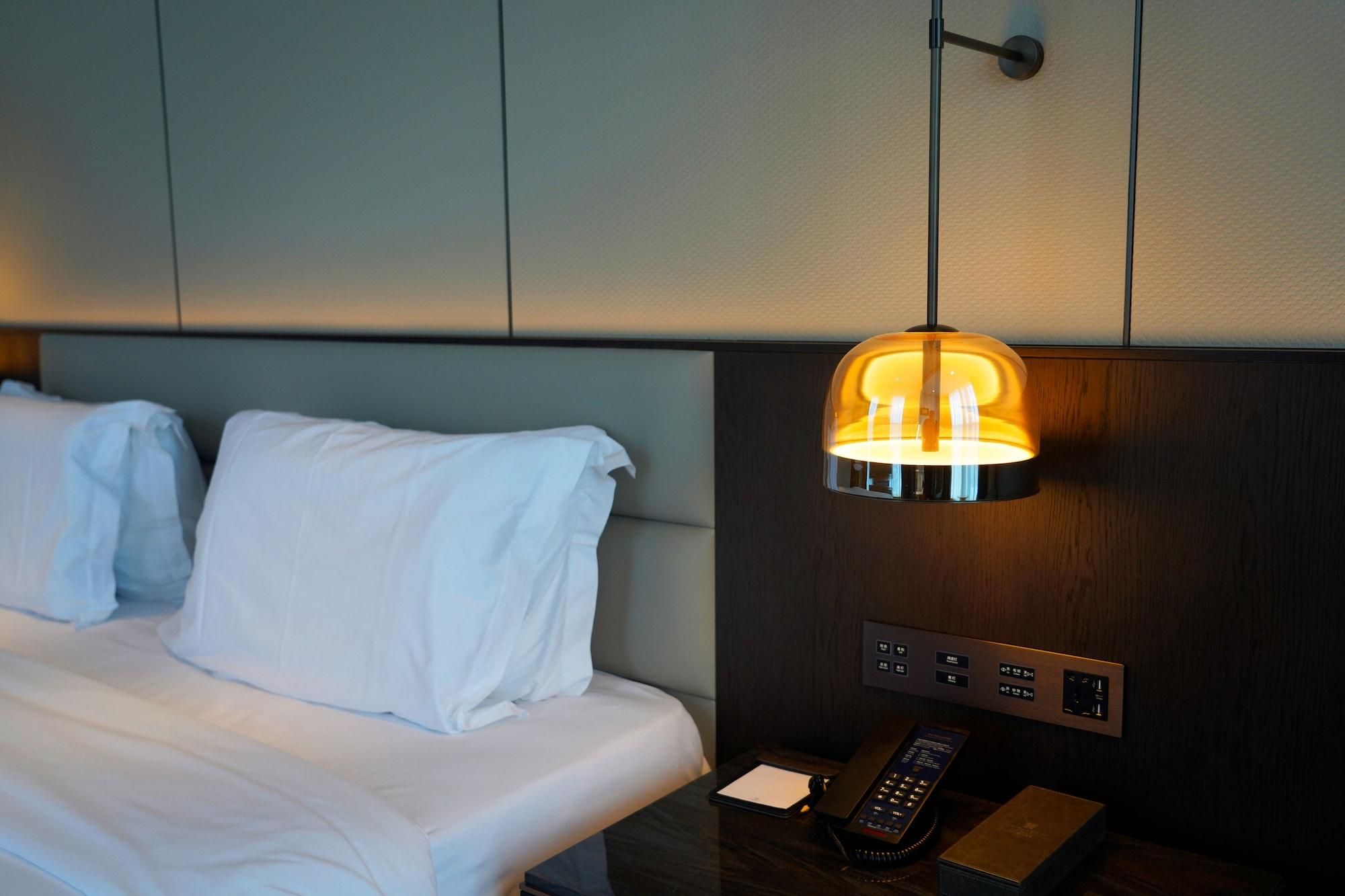 Una habitación de hotel con cama, una mesita de noche con control remoto y una lámpara de pared.