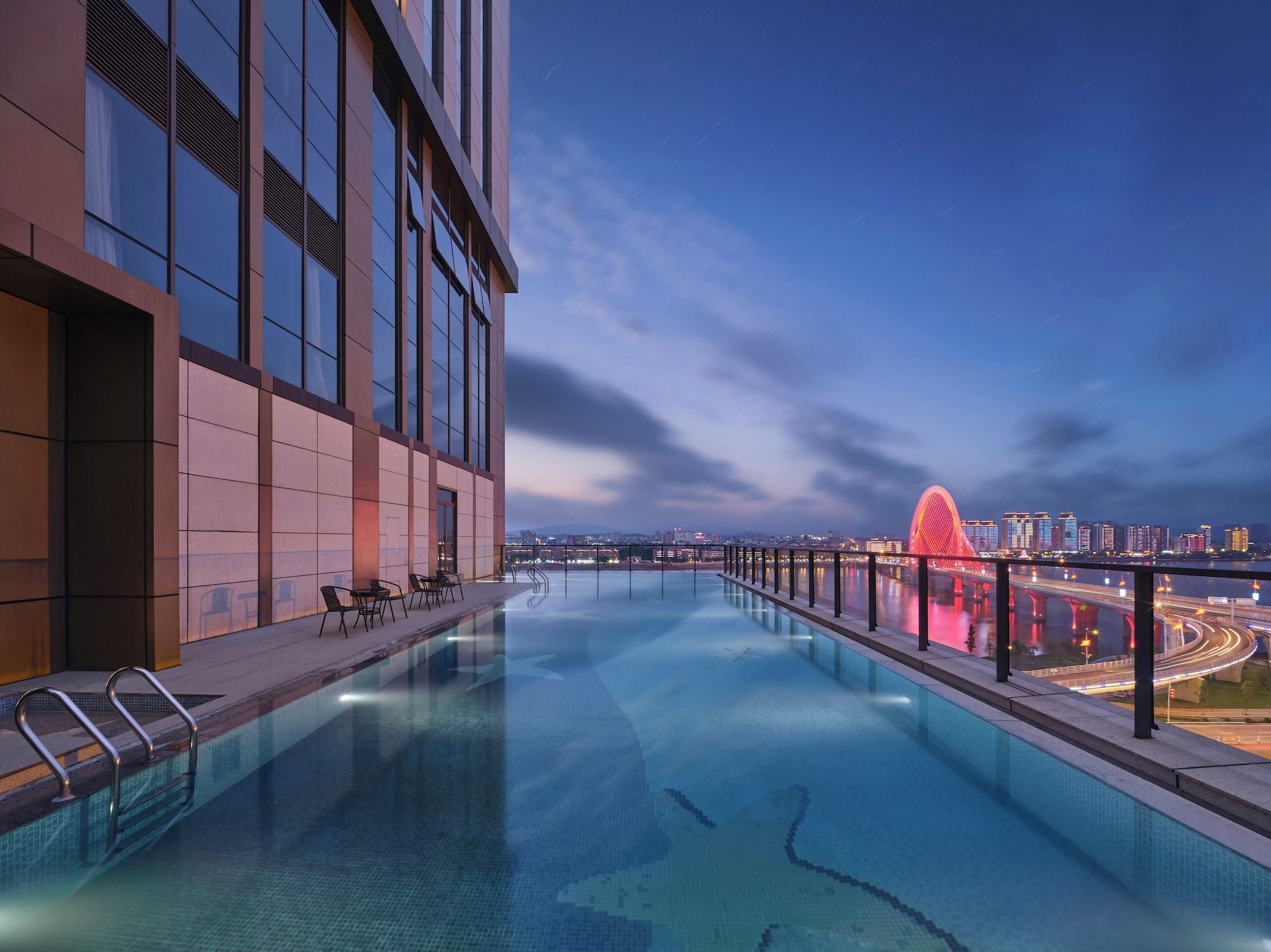 A rooftop infinity pool with a city view, modern architecture, and a red bridge in the background.