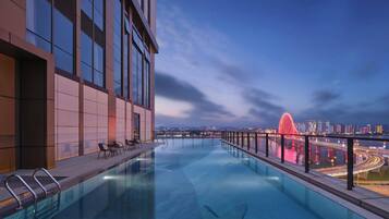 A rooftop infinity pool with a city view, modern architecture, and a red bridge in the background.