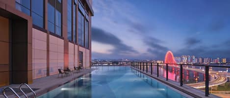 A rooftop infinity pool with a city view, modern architecture, and a red bridge in the background.