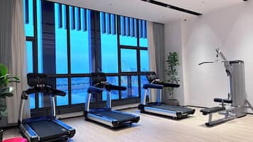 A modern gym with treadmills, a bench press, and a large window with a city view.