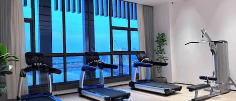 A modern gym with treadmills, a bench press, and a large window with a city view.