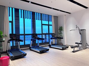 A modern gym with treadmills, a bench press, and a large window with a city view. - Wanda Realm Yudu Ganzhou (Guangzhou)