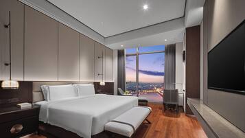 A modern hotel room with a large bed, a desk, a TV, and a view of the cityscape.
