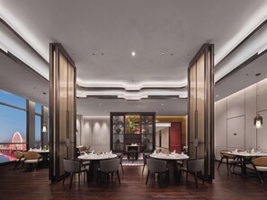 Un comedor de hotel moderno con mesas redondas, sillas y vistas a un paisaje urbano.