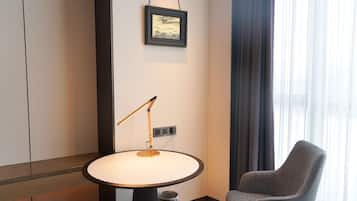 A hotel room with a round table, a single chair, a standing lamp, a power outlet, and a framed picture on the wall.