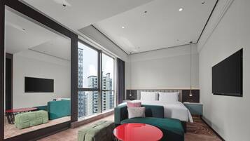 Una habitación de hotel moderna con un ventanal grande, una cama, un televisor y una mesa roja.