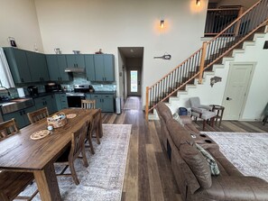 A spacious living area with a wooden dining table, a brown leather sofa, a kitchen with teal cabinets, and a wooden staircase. - Charming 2-bedroom house with Sunrise balcony views in cozy Vian (Vian)