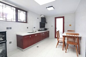 A compact kitchen with a dining area, white tiled flooring, a built-in stove, and a window with a geometric design. - Guishanju Boutique Homestay (Laishui)