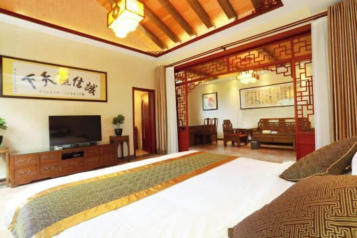 Quarto com cama, televisão, armário de madeira e um ecrã decorativo tradicional.