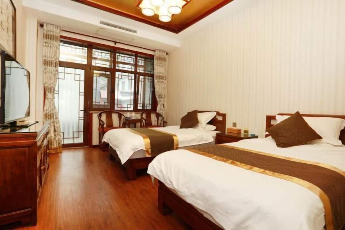 Quarto de hotel com duas camas, piso de madeira, televisão e janela com cortinas.