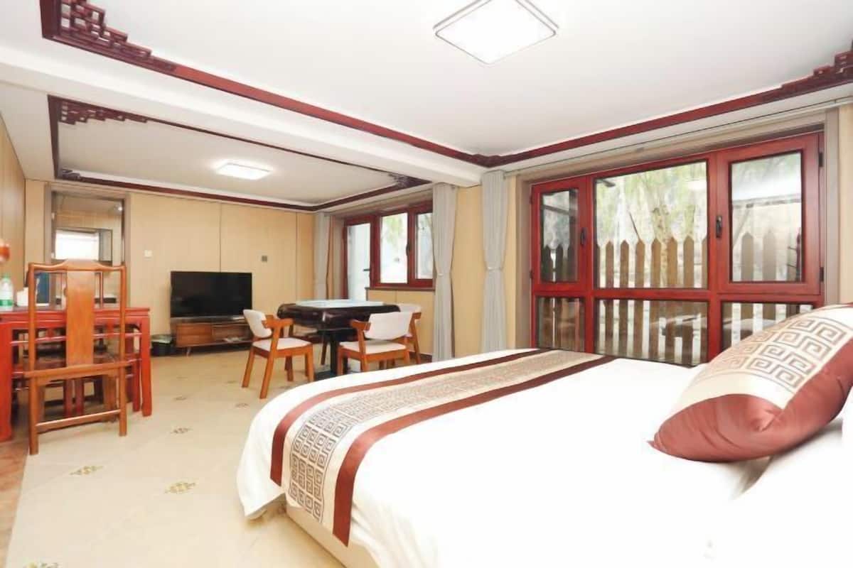 Quarto de hotel com cama, escrivaninha, televisão e janela com vista para uma cerca.