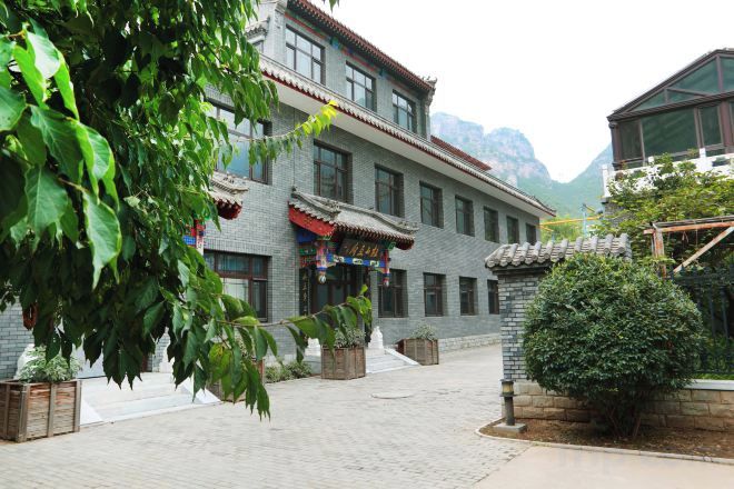 A traditional building with a tiled roof, a courtyard with potted plants, and a mountainous backdrop.