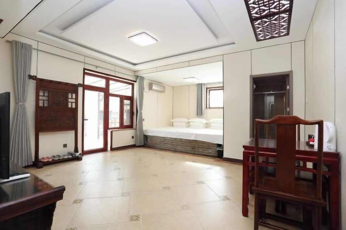 Quarto com televisão, cadeira de madeira, cama com almofadas e janela.