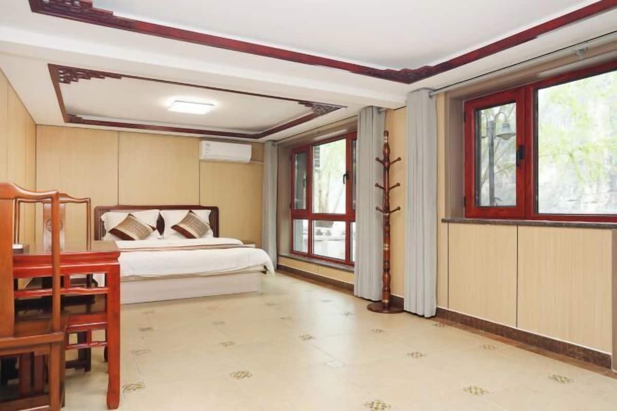 Quarto com cama, uma cadeira de madeira, janela com cortinas e teto com iluminação embutida.