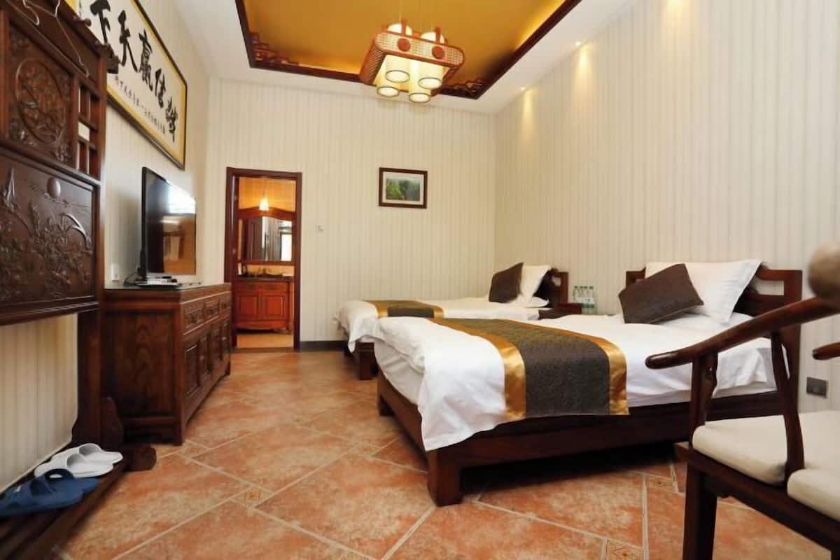 Quarto de hotel com cama, escrivaninha, cadeira e televisão.