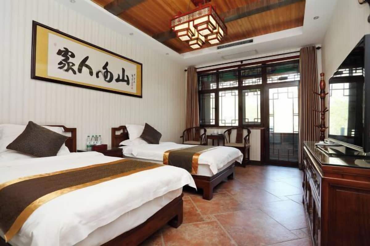 Quarto de hotel com duas camas, uma televisão, um armário de madeira e uma janela grande com cortinas.