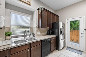 Una cocina con armarios de madera oscura, electrodomésticos de acero inoxidable y una ventana con persianas.