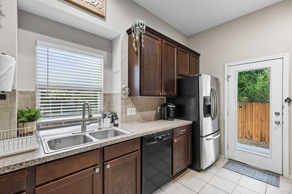 A kitchen with a stainless steel refrigerator, a dishwasher, and a sink with a window above. - Spacious 5-bd/3-ba Forest View Getaway (Dallas)