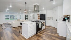 Une cuisine moderne avec des meubles blancs, un îlot central doté d’une cuisinière et un coin repas avec un canapé blanc.