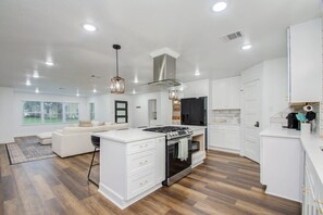 A modern kitchen with white cabinetry, a central island, and a dining area with a white sofa. - 3 Beds Houston Home, Close NRG Stadium & Rodeo (Houston)
