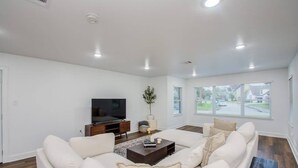 Un salon moderne avec un grand canapé, une table basse, un téléviseur à écran plat et une fenêtre donnant sur la rue.