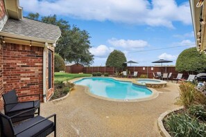A backyard with a swimming pool, a brick house, and outdoor furniture. - Modern, Spacious - Pool & Backyard Oasis & Cinema (Rowlett)