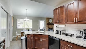 A modern kitchen with wooden cabinets, a dishwasher, a coffee maker, and a dining area with a table and chairs. - Texan Hideaway - Cozy, Convenient, Comfortable! (Lewisville)