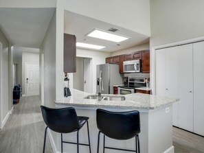 A modern kitchen with a central island, bar stools, and a microwave. - Texan Hideaway - Cozy, Convenient, Comfortable! (Lewisville)