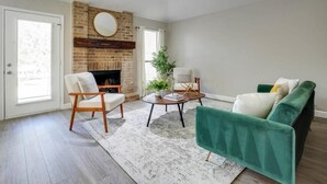 A living room with a fireplace, a ceiling fan, and a green sofa. - Texan Hideaway - Cozy, Convenient, Comfortable! (Lewisville)