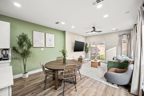 A modern living room with a dining table, chairs, a sofa, a TV, and a large window. - Bright Modern & Cheerful 3bd/3ba, Medical District (Dallas)