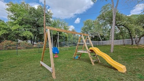 A wooden swing set with a yellow slide in a grassy yard. - Your Rustic Retreat w Backyard Oasis, Pool, Patio (Roanoke)