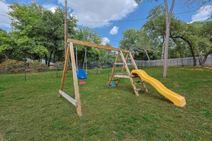 A wooden swing set with a yellow slide in a grassy yard. - Your Rustic Retreat w Backyard Oasis, Pool, Patio (Roanoke)