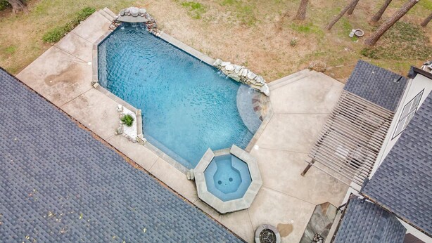 A rectangular swimming pool with a hot tub, surrounded by a stone border and a concrete deck. - Your Rustic Retreat w Backyard Oasis, Pool, Patio (Roanoke)