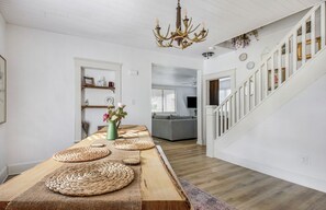 Una habitación amplia con una mesa de comedor de madera, una araña y una escalera que lleva a otra zona.