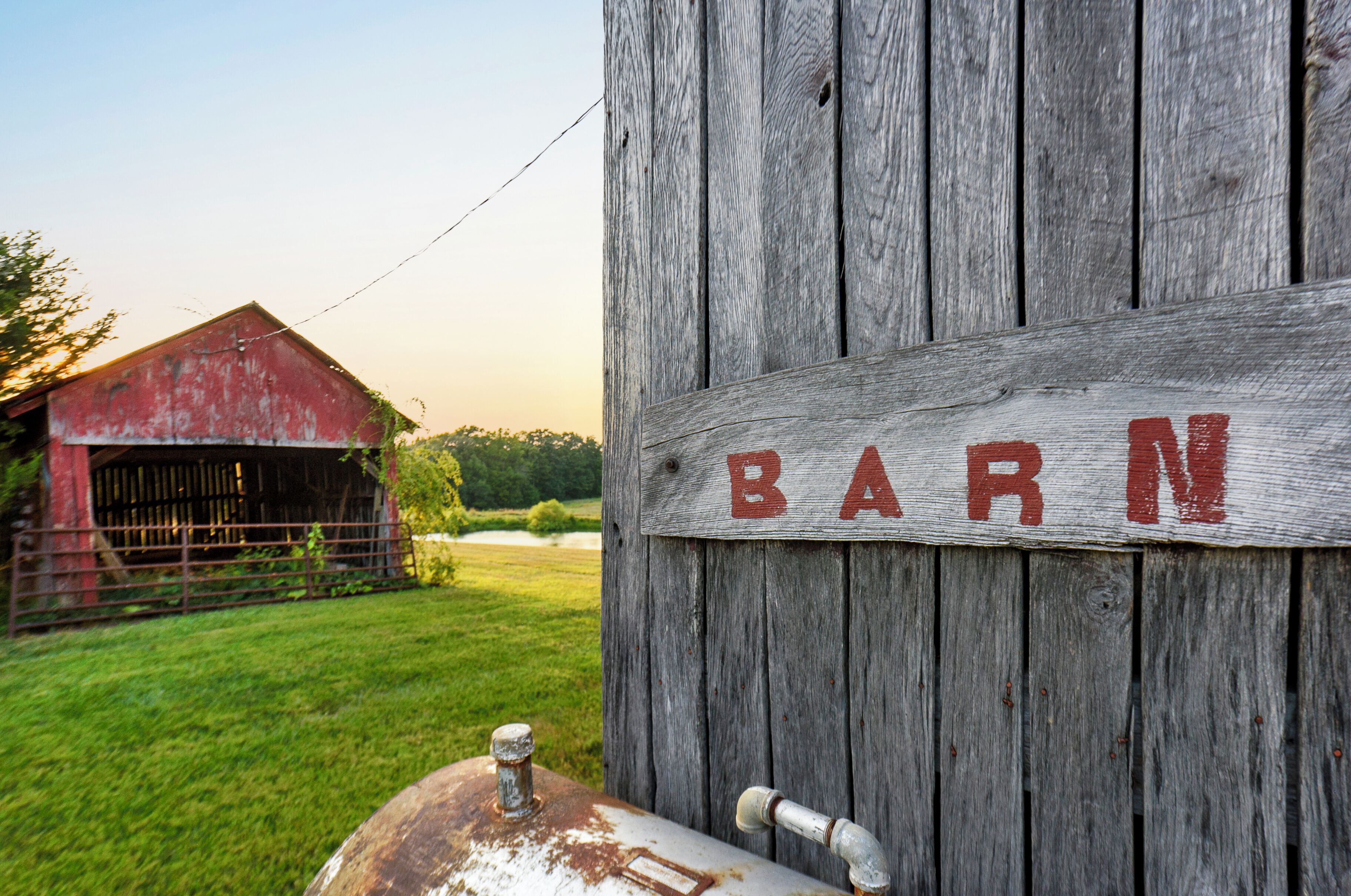 A rustic barn with a wooden sign that reads 'BARN' and a metal structure in the foreground.