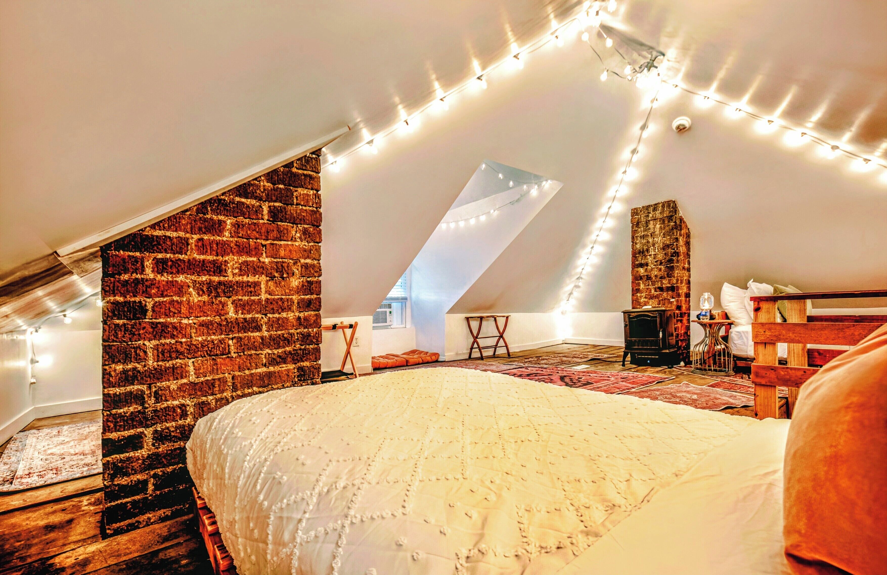 A loft bedroom with a sloped ceiling, exposed brick wall, and string lights.