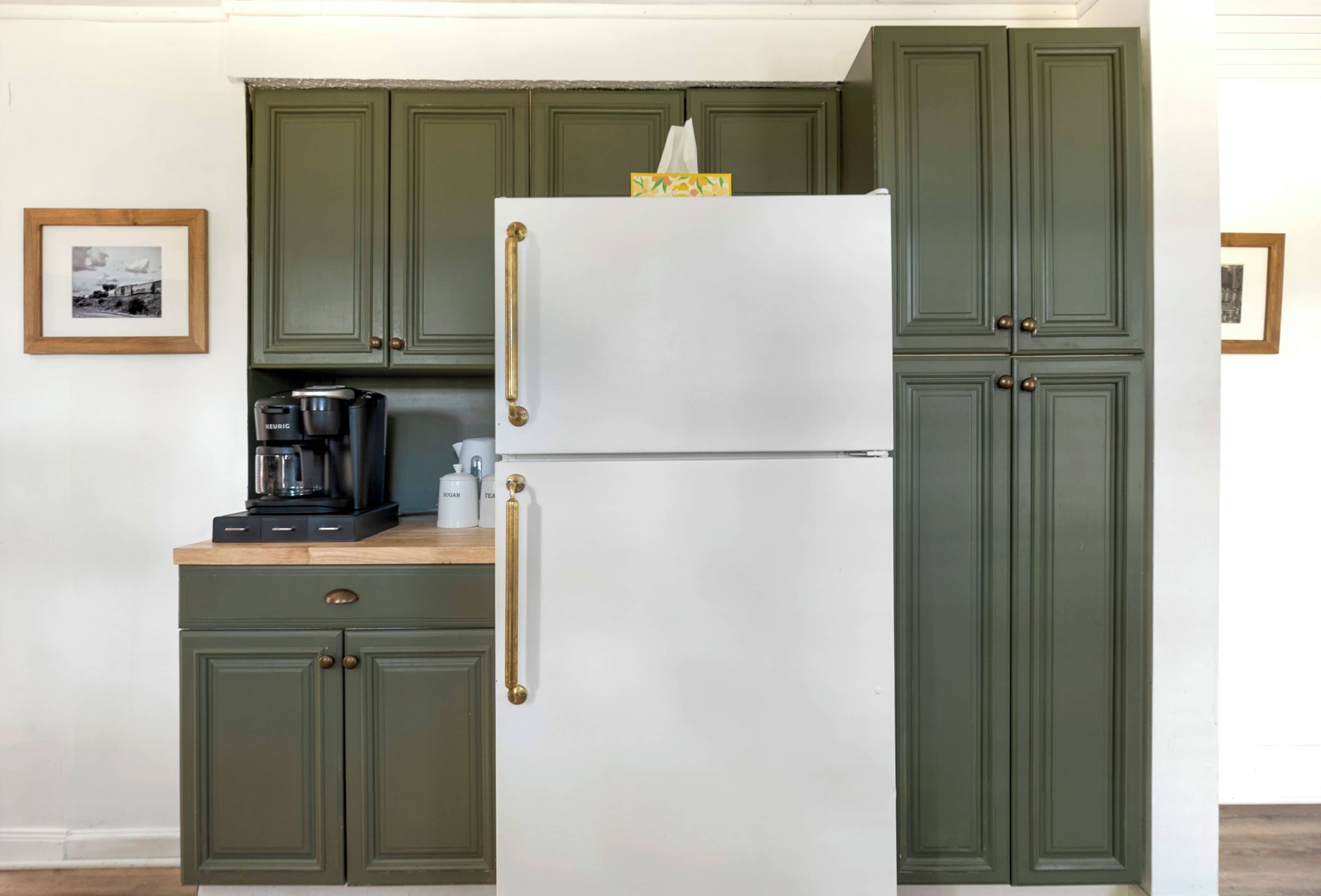 Una cocina con armarios verdes, un refrigerador blanco y una cafetera sobre la encimera.