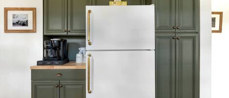 Una cocina con armarios verdes, un refrigerador blanco y una cafetera sobre la encimera.