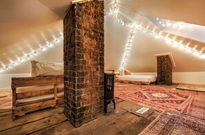 A loft bedroom with a sloped ceiling, exposed brick walls, a wooden bench, a small black heater, and a patterned rug. - Hocking Hills Retreat with Sauna, Hot Tub, Movie Theater, Fire Pit (McArthur)