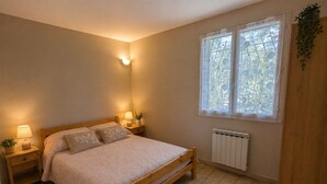 Ein Schlafzimmer mit einem hölzernen Bett, Nachttischlampen, einem Heizkörper und einem Fenster mit Blick auf Grünflächen.