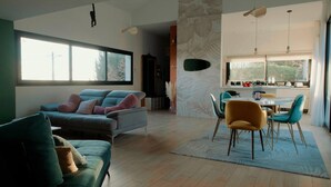 A modern living room with a sofa, chairs, a dining area with a table and chairs, and a kitchen visible through an open door. - Exceptional villa | Private pool and suites (Juville)