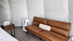A room with a brown sofa, a small bedside table, and a white air purifier. - Riverfront Dome Retreat | Private Bath + Views (Calgary)