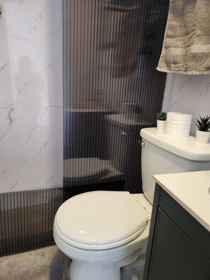 A bathroom with a toilet, a shower enclosure, a marble wall, and a towel rack.