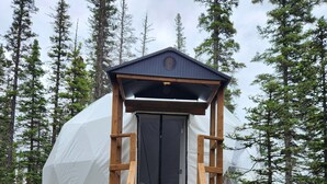 A wooden staircase leading to a covered entrance of a cabin-like structure surrounded by trees. - Riverfront Dome Retreat | Private Bath + Views (Calgary)