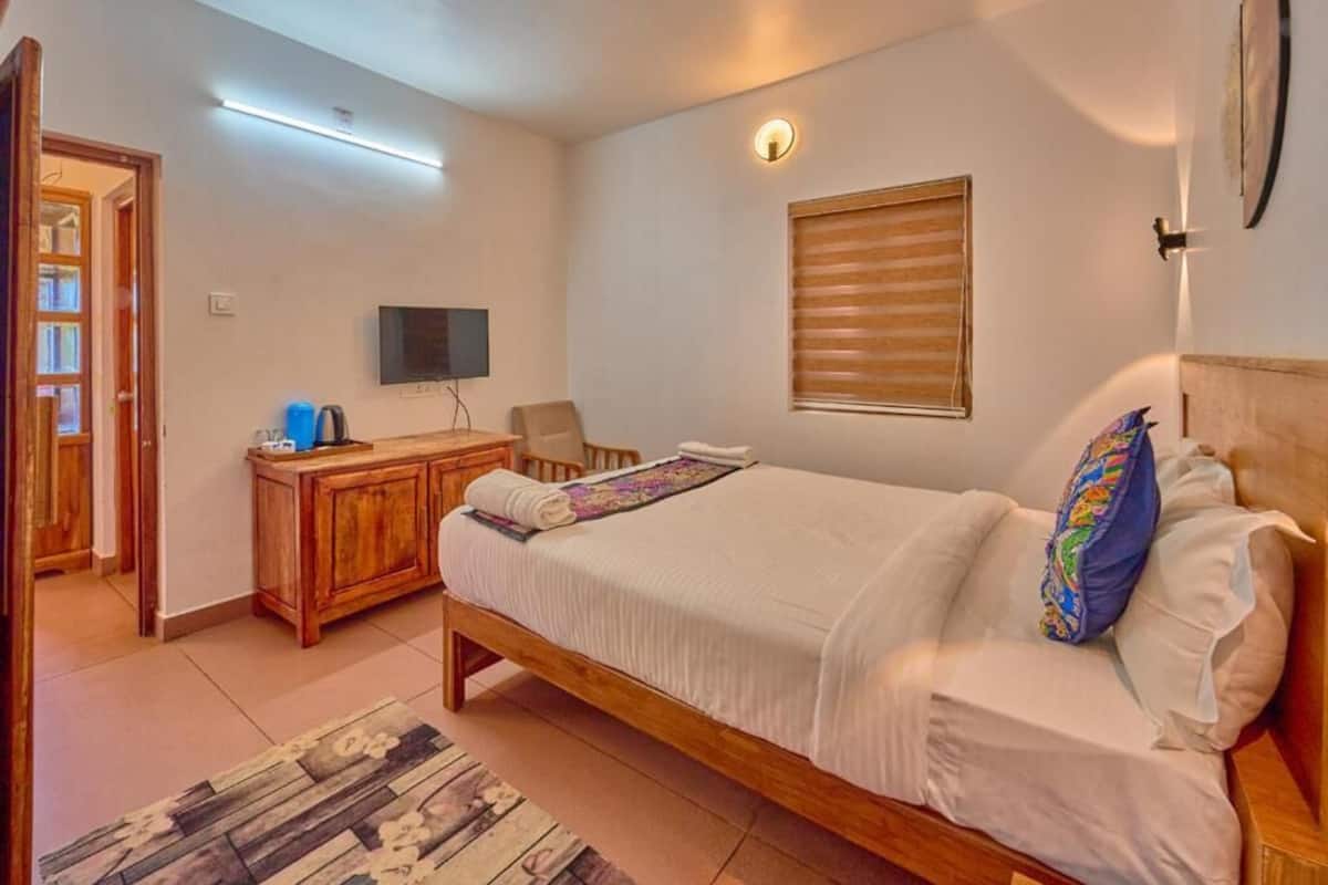 A bedroom with a wooden bed, a television, a desk, and a window with blinds.